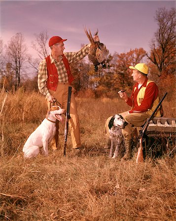 simsearch:846-02797725,k - 1960s TWO MEN HUNTERS SITTING STANDING WITH HUNTING DOGS HOLDING BRACE OF HARVESTED PHEASANT Stock Photo - Rights-Managed, Code: 846-09012908