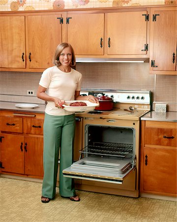 simsearch:846-02794052,k - 1970s SMILING BLOND WOMAN HOUSEWIFE LOOKING AT CAMERA HOLDING BAKED HAM STANDING BY STOVE OPEN OVEN DOOR Foto de stock - Con derechos protegidos, Código: 846-09012926