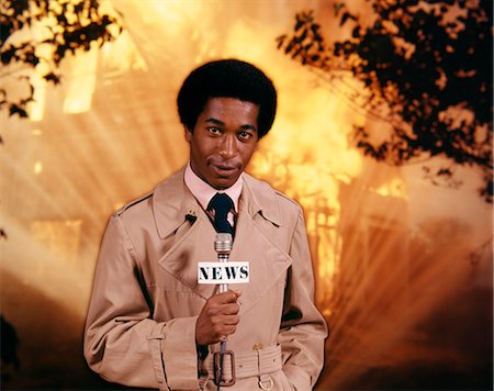 simsearch:846-05645665,k - 1970s AFRICAN AMERICAN MAN TELEVISION NEWS REPORTER WEARING RAINCOAT SPEAKING INTO MICROPHONE AT FIRE SCENE LOOKING AT CAMERA Stock Photo - Rights-Managed, Code: 846-09013035