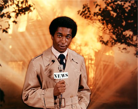 simsearch:846-02794130,k - 1970s AFRICAN AMERICAN TV NEWSMAN WEARING TRENCH COAT LOOKING AT CAMERA HOLD MICROPHONE REPORTING AT SCENE OF RAGING HOUSE FIRE Stock Photo - Rights-Managed, Code: 846-09013036