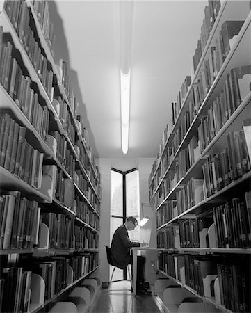 simsearch:846-08639518,k - 1960s YOUNG MAN STUDENT READING STUDYING AMONG LIBRARY BOOK STACKS Stock Photo - Rights-Managed, Code: 846-09013116