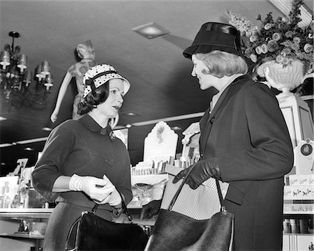 simsearch:846-08030416,k - 1960s TWO WOMEN WEARING HATS SHOPPING STANDING MEETING TALKING VISITING IN FRONT OF COSMETIC COUNTER OF DEPARTMENT STORE Stock Photo - Rights-Managed, Code: 846-09013112