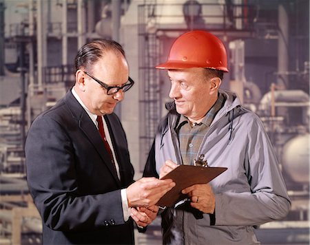 1960s EXECUTIVE AND HARD HAT ENGINEER WITH CLIPBOARD TALKING FACTORY REFINERY IN BACKGROUND OUTDOOR Stock Photo - Rights-Managed, Code: 846-09085334