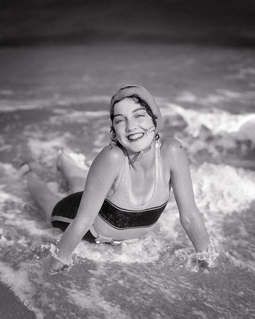 1920s SMILING BRUNETTE WOMAN LYING IN BEACH SURF WAVES WEARING BATHING CAP SWIMSUIT LOOKING AT CAMERA Stock Photo - Rights-Managed, Code: 846-09181592