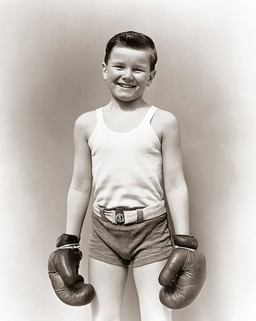 1930s SMILING BOY IN T-SHIRT AND GYM SHORTS STANDING LOOKING AT CAMERA WEARING BOXING GLOVES READY FOR A FIGHT Foto de stock - Con derechos protegidos, Código: 846-09181678