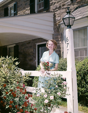 1960s SMILING WOMAN STANDING IN FRONT OF HOUSE HOLDING FLOWERS LOOKING AT CAMERA Stock Photo - Rights-Managed, Code: 846-09181779