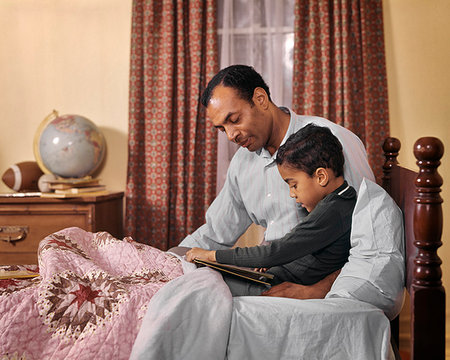 1960s 1970s AFRICAN AMERICAN MAN FATHER AND BOY SON READING BEDTIME STORYBOOK BED ROOM TOGETHER TEACHING LEARNING LOVE Stock Photo - Rights-Managed, Code: 846-09181814
