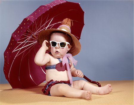 1960s BABY GIRL WEARING TWO PIECE BIKINI AND STRAW HAT SUNGLASSES SITTING BY RED BEACH UMBRELLA Stock Photo - Rights-Managed, Code: 846-02794046
