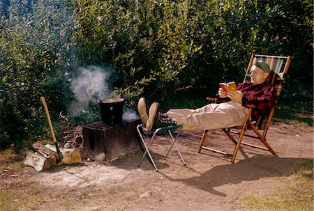 DES ANNÉES 1950 L'HOMME LECTURE SÉANCE PLIANTE CAMP PRÉSIDENT CAMPFIRE GRIL POT FUMÉE HACHE FEU BOIS PATTISON STATE PARK AU WISCONSIN Photographie de stock - Rights-Managed, Code: 846-02794088