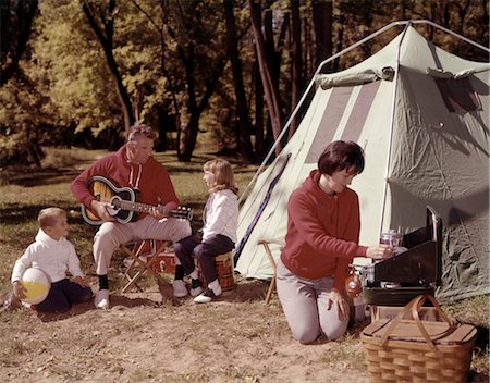 retro wife cooking - PARENTS WITH SON AND DAUGHTER OUTSIDE TENT PLAYING GUITAR AND COOKING ON GRILL FOUR MAN WOMAN BOY GIRL VACATION 1960s Stock Photo - Rights-Managed, Code: 846-02794107