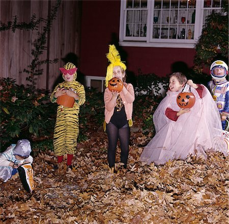 1970s GROUP OF FIVE BOYS AND GIRLS IN HALLOWEEN COSTUMES HOLDING TRICK OR TREAT PUMPKINS AND BAGS IN FRONT YARD OF HOUSE Stock Photo - Rights-Managed, Code: 846-02794392