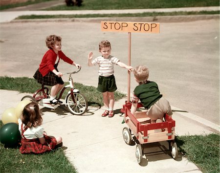 1950s BOYS AND GIRLS OUTDOOR WITH TRICYCLE AND WAGON PLAYING TRAFFIC WITH POLICE STOP SIGN AMERICANA Foto de stock - Con derechos protegidos, Código: 846-02794447