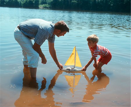 1970s FATHER AND SON PUSHING A TOY SAILBOAT IN A LAKE Stock Photo - Rights-Managed, Code: 846-02794511