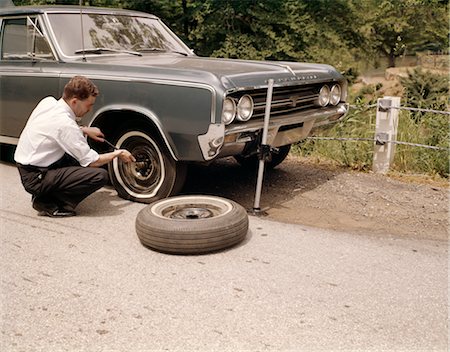 1960s MAN CHANGING FLAT TIRE ON CAR AT SIDE OF RURAL ROAD CAR JACK TOOLS TIRE IRON Stock Photo - Rights-Managed, Code: 846-02794707