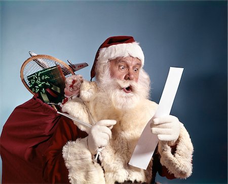 1950s 1960s 1970'S SURPRISED SANTA CLAUS CARRYING SACK OF TOYS READING LIST STUDIO INDOOR Stock Photo - Rights-Managed, Code: 846-02795287