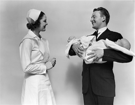 1930s 1940s SMILING WOMAN NURSE TALKING WITH MAN PROUD NEW FATHER HOLDING NEWBORN TWIN BABIES Stock Photo - Rights-Managed, Code: 846-02795686