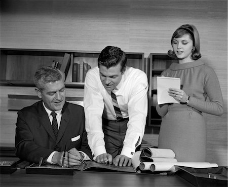 1960s PAIR OF BUSINESSMEN BEHIND DESK LOOKING AT BLUEPRINTS WITH SECRETARY AT SIDE TAKING NOTES Stock Photo - Rights-Managed, Code: 846-02795837