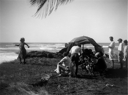 1920s MOVIE CREW FILMING WOMAN IN GRASS SKIRT HULA DANCING ALONG SHORE Stock Photo - Rights-Managed, Code: 846-02795873