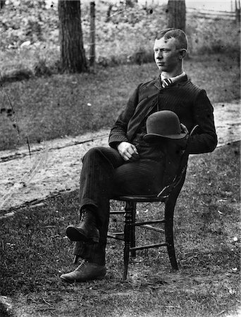 1890s 1900s SIDE VIEW OF MAN WEARING SUIT SEATED ON CHAIR OUTSIDE HOLDING BOWLER HAT Stock Photo - Rights-Managed, Code: 846-02795913