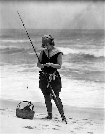 swimming suit woman old photo - 1920s WOMAN IN BATHING SUIT COSTUME STANDING ON BEACH PUTTING BAIT ON SURF FISHING POLE Stock Photo - Rights-Managed, Code: 846-02795937