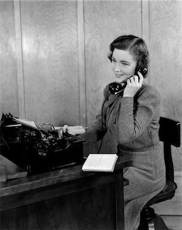 1940s SMILING YOUNG WOMAN SECRETARY RECEPTIONIST SITTING AT OFFICE DESK TALKING ON TELEPHONE Foto de stock - Con derechos protegidos, Código: 846-02795949