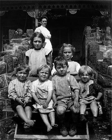 1890s 1900s TURN OF THE CENTURY GROUP OF SIX DIRTY CHILDREN SITTING ON STAIRS IN FRONT OF HOUSE WITH MOTHER STANDING ON PORCH IN BACKGROUND Stock Photo - Rights-Managed, Code: 846-02795986