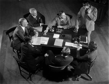 1930s SIX MEN AND ONE WOMAN SITTING AROUND OFFICE DESK WHILE ONE MAN TALKS ON TELEPHONE Stock Photo - Rights-Managed, Code: 846-02796046
