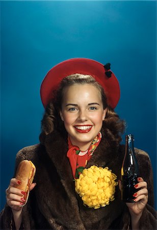 1940s 1950s SMILING TEENAGE HIGH SCHOOL COLLEGE GIRL HOLDING HOT DOG AND SODA POP BOTTLE WEARING FUR COAT AND BIG YELLOW HOMECOMING FOOTBALL GAME CHRYSANTHEMUM Stock Photo - Rights-Managed, Code: 846-02796119