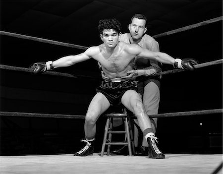 1950s BOXER IN RING WITH COACH TRAINER HOLDING HIM BACK ARMS STRETCHED HOLDING ROPES ON EITHER SIDE DETERMINED AGGRESSIVE Stock Photo - Rights-Managed, Code: 846-02796195