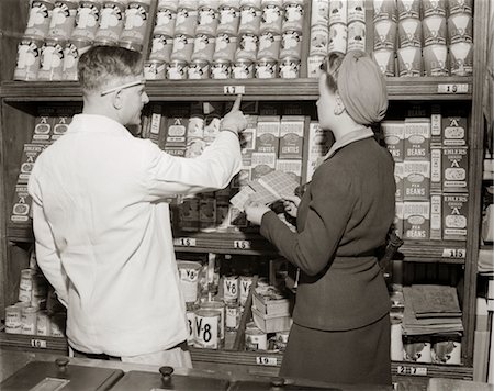 simsearch:846-02796799,k - 1940s BACK VIEW OF GROCER POINTING OUT PRICES OF CANNED GOODS TO WOMAN HOLDING RATION BOOK Stock Photo - Rights-Managed, Code: 846-02796351