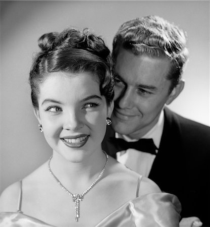 1950s 1960s SMILING HAPPY COUPLE WOMAN DIAMOND NECKLACE EARRINGS MAN BEHIND HER WEARING TUXEDO FORMAL EVENING ATTIRE Stock Photo - Rights-Managed, Code: 846-02796715