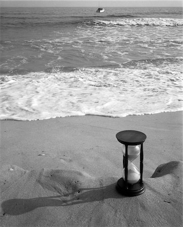 1960s SET-UP OF HOURGLASS ON LEDGE OF SAND WITH WAVES WASHING UP ON SHORE & BOAT COMING IN BACKGROUND Stock Photo - Rights-Managed, Code: 846-02796962