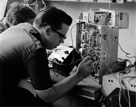 1960s SIDE VIEW OF STUDENTS WORKING ON CIRCUITRY PANEL WITH SMALL SOLDERING IRON Foto de stock - Con derechos protegidos, Código: 846-02797031