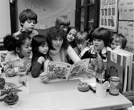 1980s TEACHER READING BOOK TO GROUP OF GRADE SCHOOL STUDENTS GATHERED AROUND HER Stock Photo - Rights-Managed, Code: 846-02797152