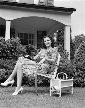 ANNÉES 1940 FEMME TENANT UN LIVRE SOURIANT À LA CAMÉRA ASSIS DANS LA MAISON DE PORCHE DE PELOUSE CHAISE MAGAZINE RACK Photographie de stock - Rights-Managed, Code: 846-02797549