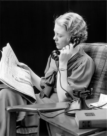 1920s 1930s YOUNG WOMAN SITTING IN CHAIR LOOKING AT NEWSPAPER TALKING ON TELEPHONE Stock Photo - Rights-Managed, Code: 846-02797603