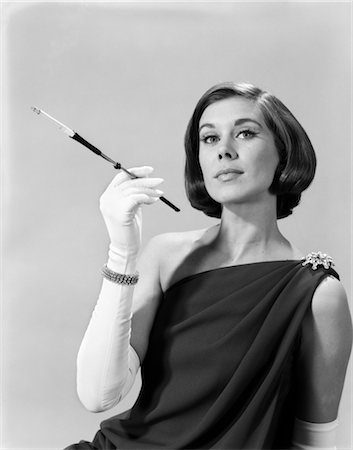 1960s FORMALLY ELEGANTLY DRESSED YOUNG WOMAN ARROGANT EXPRESSION HOLDING LONG CIGARETTE HOLDER WEARING LONG WHITE GLOVES Stock Photo - Rights-Managed, Code: 846-02797697