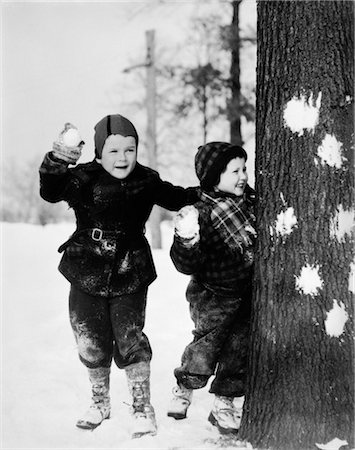 1930s TWO BOYS PLAYING IN THE SNOW HIDING BEHIND TREE WITH SNOWBALLS IN HANDS HAVE A SNOWBALL FIGHT Stock Photo - Rights-Managed, Code: 846-02797761