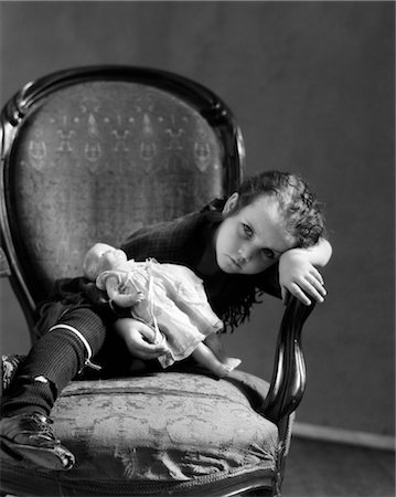 poor - 1930s GIRL IN TATTERED CLOTHING SITTING HOLDING BABY DOLL LEANING HEAD ON ARM OF CHAIR WITH SAD EXPRESSION Stock Photo - Rights-Managed, Code: 846-02797788