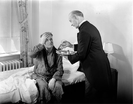 1930s 1940s MAN SIT ON BED HAND TO HEAD DOCTOR BUTLER WITH TRAY MIXING POWDER IN GLASSES HEADACHE HANGOVER PAIN Stock Photo - Rights-Managed, Code: 846-02791719