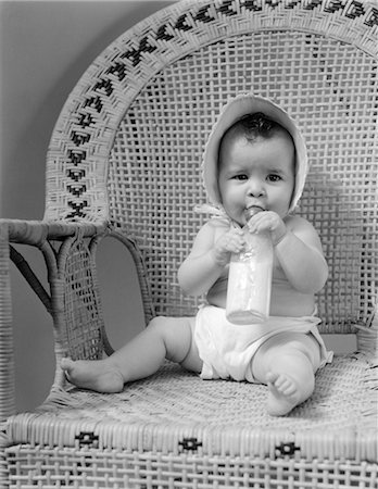 simsearch:846-02796799,k - 1930s BABY SITTING IN WICKER CHAIR SUCKING MILK BOTTLE Stock Photo - Rights-Managed, Code: 846-02791933