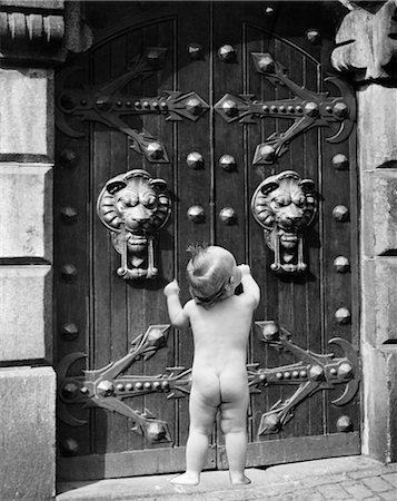 NAKED NUDE BABY FROM BACK STANDING KNOCKING ON LARGE ORNATE CASTLE DOORS LION HEAD DOOR KNOCKER METAL IRON HINGES ENTRY ENTRANCE Stock Photo - Rights-Managed, Code: 846-02792014