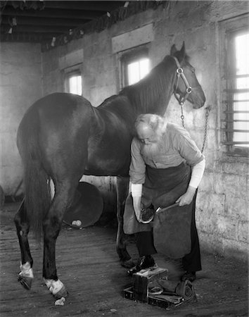 1930s ELDERLY BEARDED BLACKSMITH HOLDING HORSE'S HOOF BETWEEN LEGS & HAMMER IN OTHER HAND Foto de stock - Con derechos protegidos, Código: 846-02792220