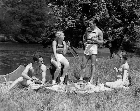 1930s TWO COUPLES HAVING SUMMER PICNIC WITH FOOD AND DRINK SPREAD OUT ON BLANKET THE TIP OF A CANOE IS VISIBLE Stock Photo - Rights-Managed, Code: 846-02792275