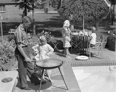 1960s FAMILY OF 5 ON THE PATIO FATHER IS GRILLING AS DAUGHTER WATCHES MOTHER SET UMBRELLA COVERED TABLE Stock Photo - Rights-Managed, Code: 846-02792308
