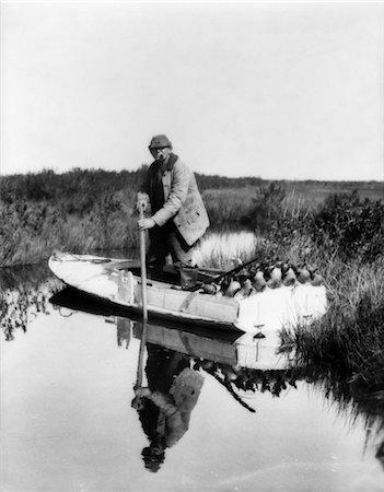decoy - 1930s 1940s SENIOR MAN STEERING SMALL BOAT FULL OF DUCK DECOYS SHOTGUN HUNTER HUNTING Stock Photo - Rights-Managed, Code: 846-02792447