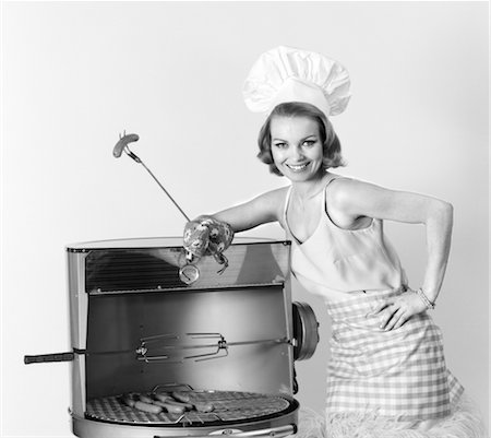 1960s WOMAN WEARING CHEF HAT STANDING AT BBQ GRILL HOLDING A FORK WITH HOT DOG Foto de stock - Con derechos protegidos, Código: 846-02792729