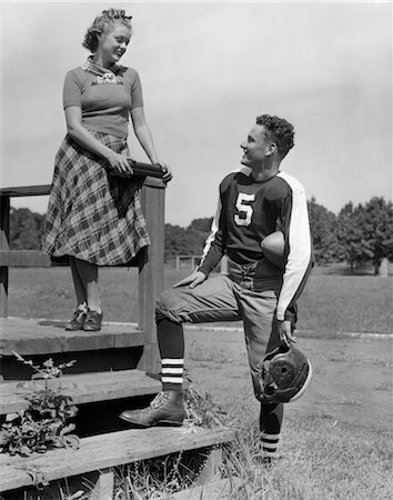 1930s 1940s YOUNG TEENAGE FOOTBALL PLAYER TALKING TO TEENAGE GIRL ON BLEACHER STEPS Foto de stock - Con derechos protegidos, Código: 846-02792831