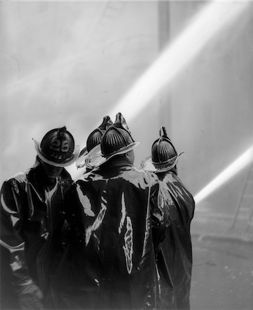1920s REAR VIEW OF FOUR FIREMEN IN BLACK SLICKERS SQUIRTING TWO HOSES Stock Photo - Rights-Managed, Code: 846-02792849