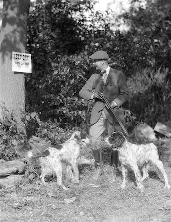simsearch:846-02797725,k - 1940s MAN WITH TWO DOGS HOLDING RIFLE READING SIGN ON TREE SAYING KEEP OFF HUNTING FASHION TRESPASSING CAP Stock Photo - Rights-Managed, Code: 846-02793047